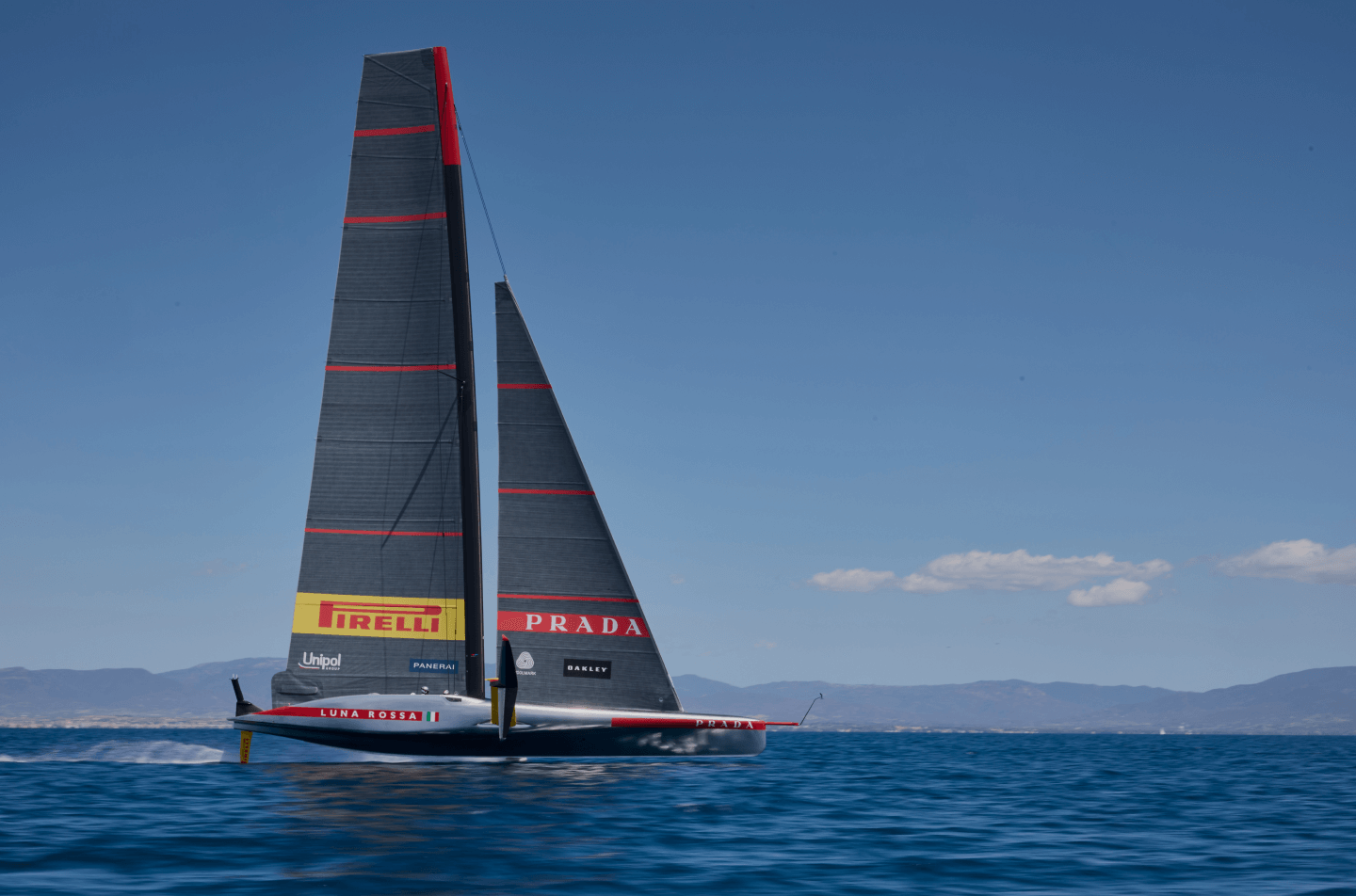 The caravel Luna Rossa sailing on the high seas with the Pirelli logo displayed and cloudy skies in the background.
