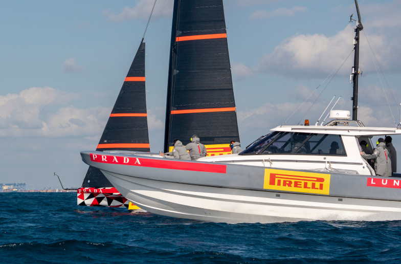 Una barca appoggio del team Pirelli Luna Rossa al fianco delle caravelle in alto mare.